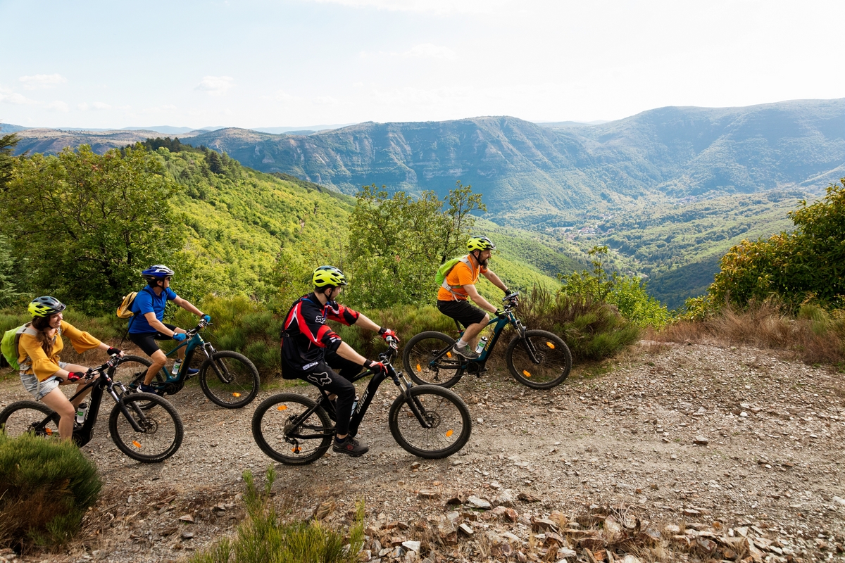 sur une piste surplombant la vallée, un groupe de 4 VTT électriques roule en admirant les causses et  Cévennes