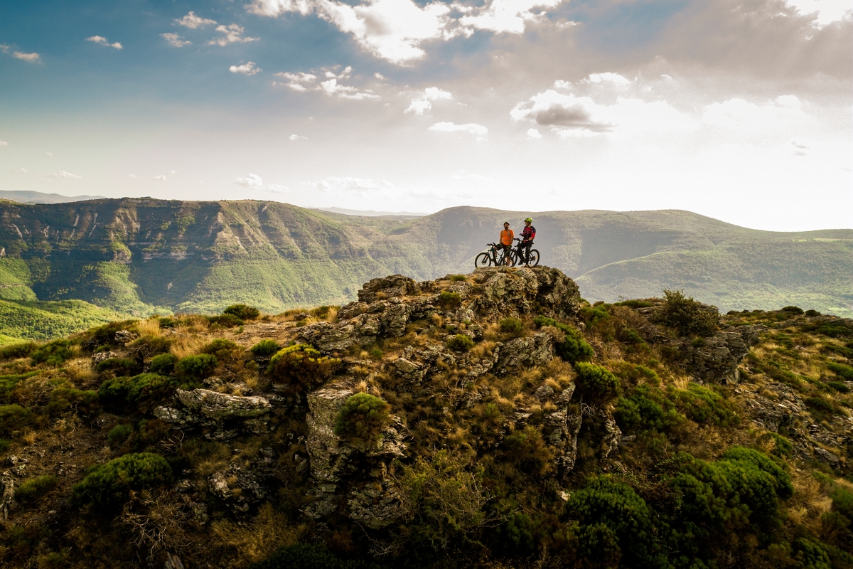 Perchés sur un piton rocheux avec les Cévennes en arrière plan, deux vététistes discutent de leur itinéraire VTT.