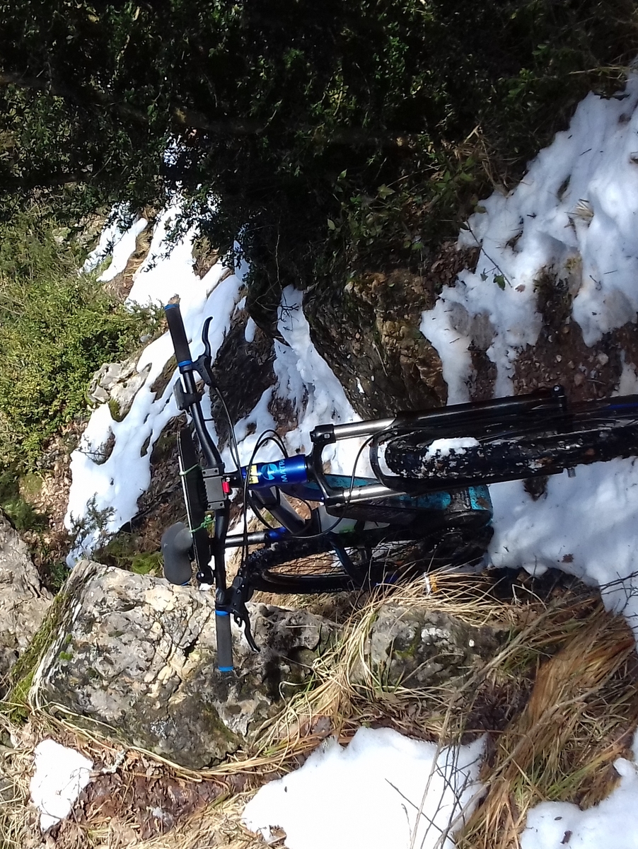 un VTT à l'arrêt dans une montée étroite et technique, avec des plaques de neige autour