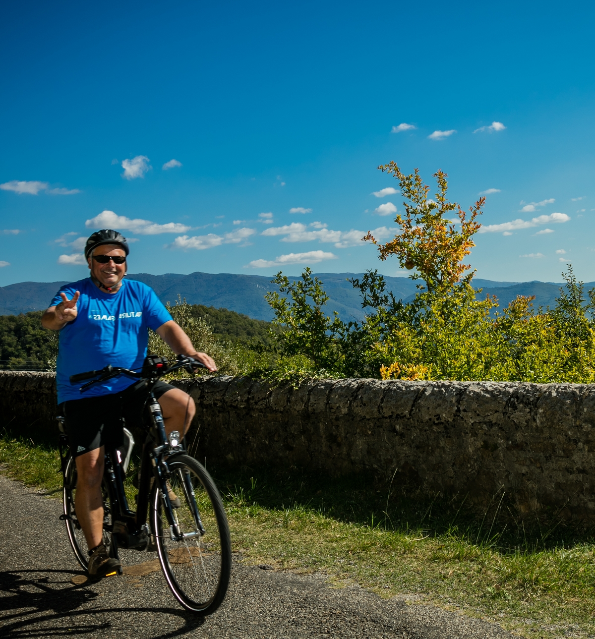 un cycliste en vélo électrique monte une pente avec un grand sourire et fait un V avec ses doigts